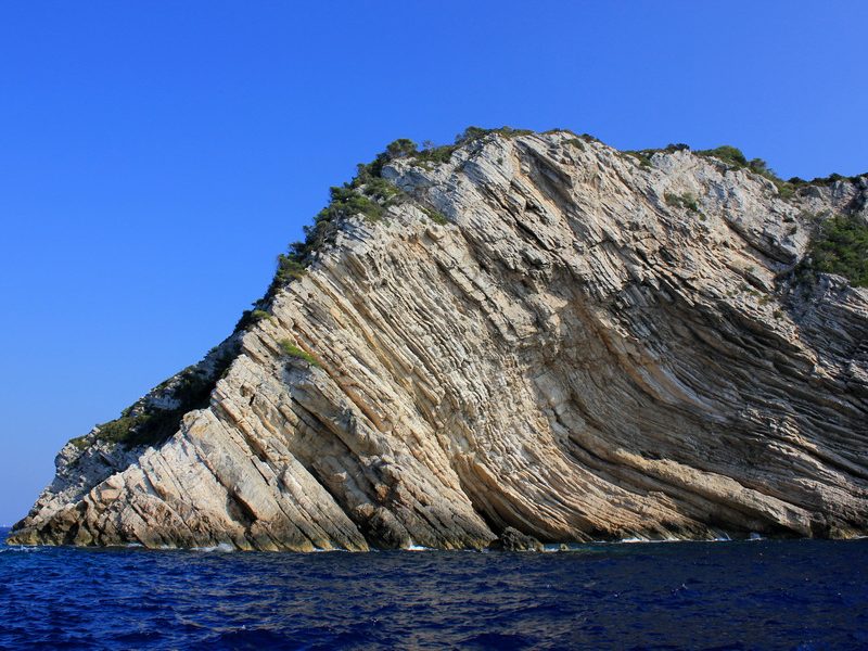 A dramatic view of the rugged coastline of Biševo island, Croatia, with steep cliffs and clear blue waters.