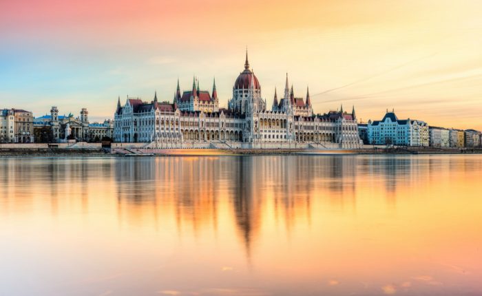 A stunning view of the Hungarian Parliament Building in Budapest, illuminated by the setting sun and reflected in the Danube River.