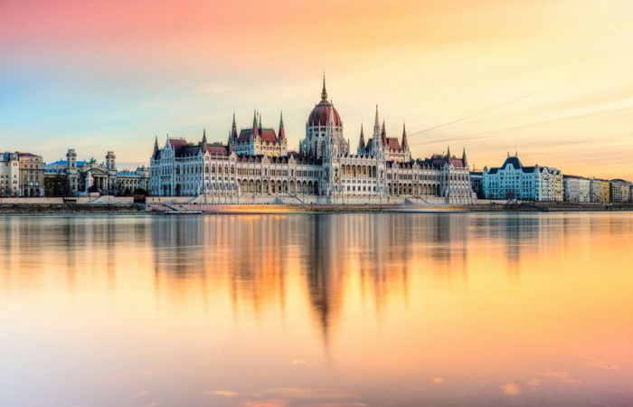 A stunning view of the Hungarian Parliament Building in Budapest, illuminated by the setting sun and reflected in the Danube River.