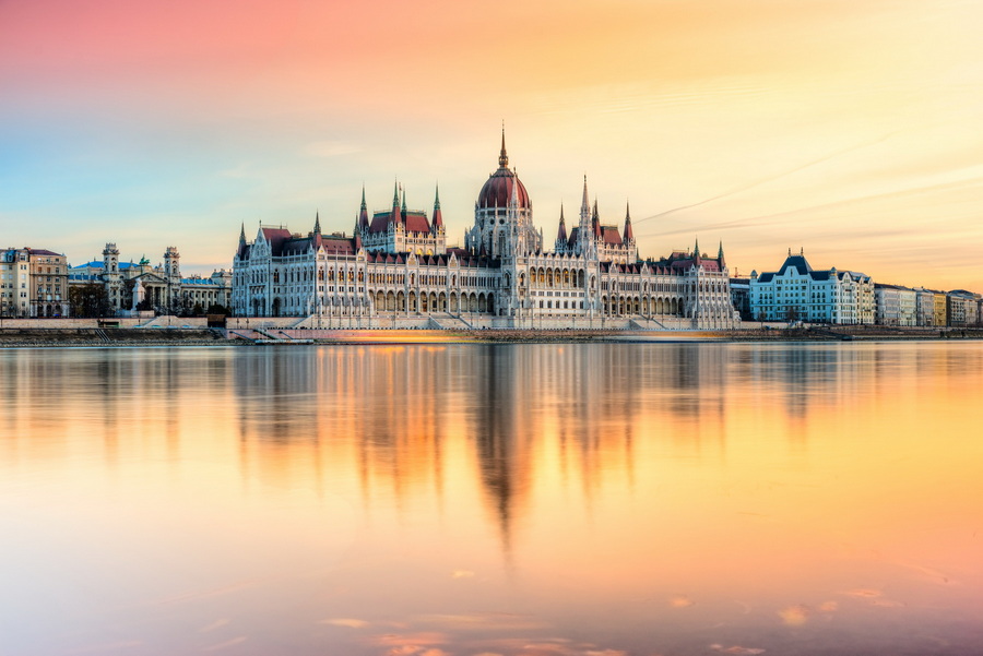 A stunning view of the Hungarian Parliament Building in Budapest, illuminated by the setting sun and reflected in the Danube River.