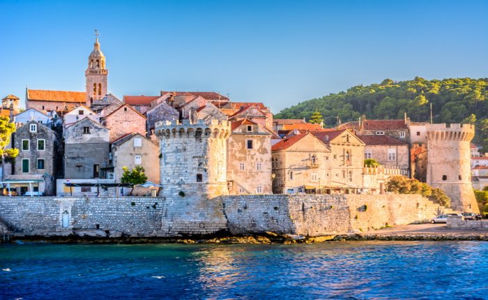 A panoramic view of Korčula's Old Town, showcasing its medieval architecture, the city walls, and the vibrant waterfront scene with people strolling along the promenade.