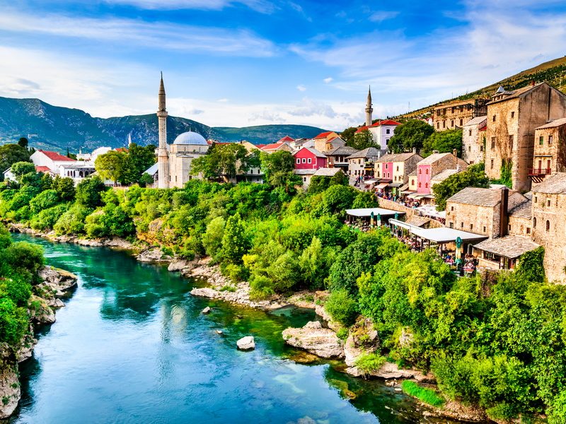 A stunning view of the Old Town of Mostar at sunset, with the iconic Stari Most bridge reflecting in the Neretva River.