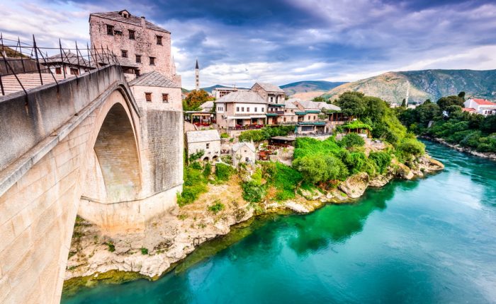 A panoramic view of the Old Bridge in Mostar, showcasing its elegant arch and the surrounding Ottoman-era architecture, with the Neretva River flowing through the city.