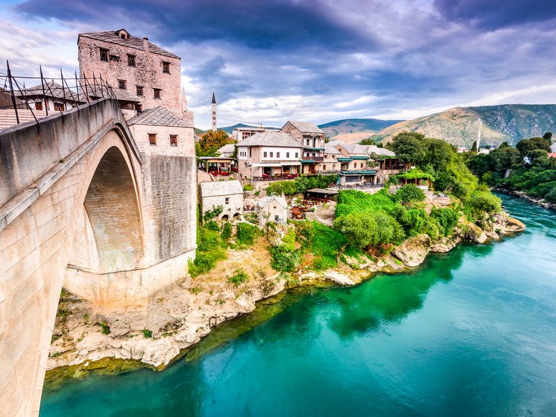 A panoramic view of the Old Bridge in Mostar, showcasing its elegant arch and the surrounding Ottoman-era architecture, with the Neretva River flowing through the city.