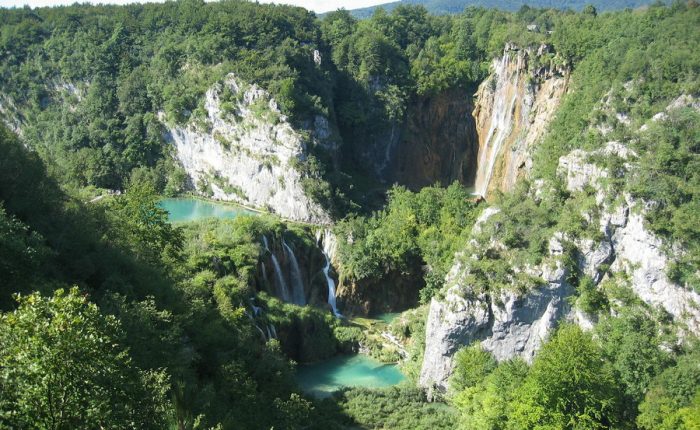 A stunning aerial view of Plitvice Lakes, with turquoise lakes nestled among towering cliffs and dense forests.