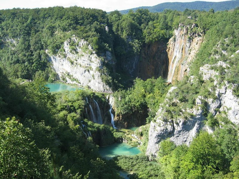 A stunning aerial view of Plitvice Lakes, with turquoise lakes nestled among towering cliffs and dense forests.