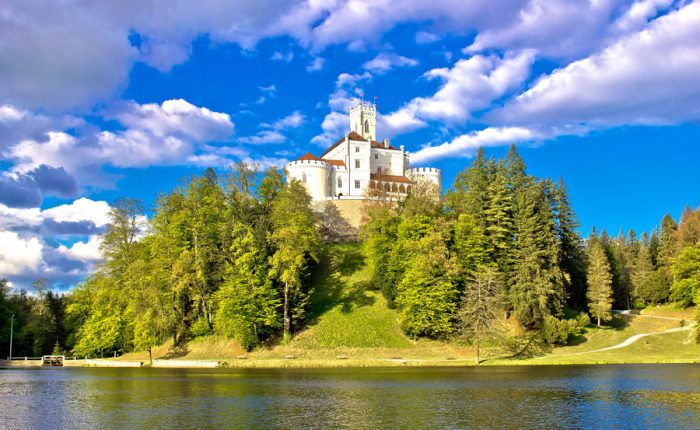 A charming castle, Trakošćan, nestled among trees on a hill overlooking a lake in Croatia.