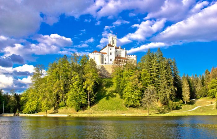 A charming castle, Trakošćan, nestled among trees on a hill overlooking a lake in Croatia.