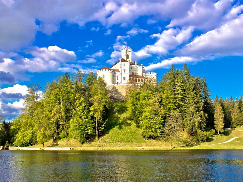 A charming castle, Trakošćan, nestled among trees on a hill overlooking a lake in Croatia.