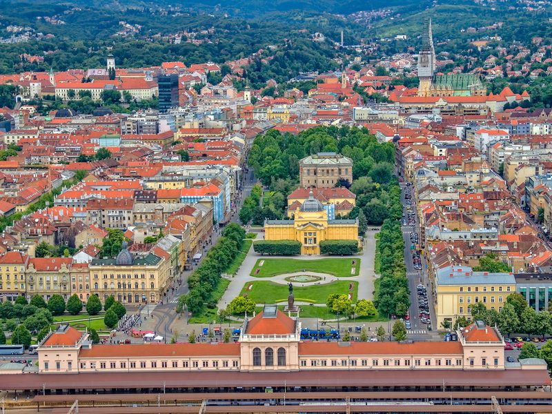 An aerial view of Zagreb, Croatia, showcasing the city's historic center, including the Main Railway Station and a park.