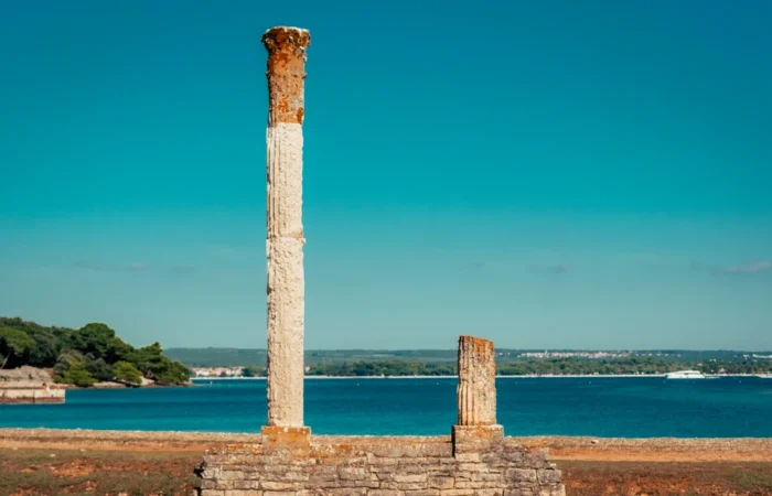 Ancient Roman ruins and weathered columns by the sea on Brijuni Island, Croatia, with turquoise water and distant coastline - historic landmark and tranquil UNESCO attraction in Istria.