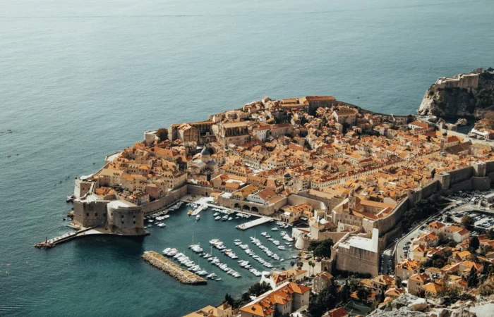 Aerial view of Dubrovnik’s UNESCO-listed Old Town encircled by medieval stone walls, with Fort Bokar, the old harbor, and terracotta rooftops beside the Adriatic Sea.