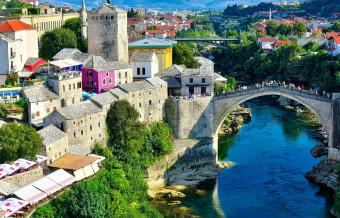 Colorful view of Mostar’s Old Bridge (Stari Most) arching over the emerald Neretva River, with historic stone houses, minarets, and lively terraces in the heart of Bosnia and Herzegovina.