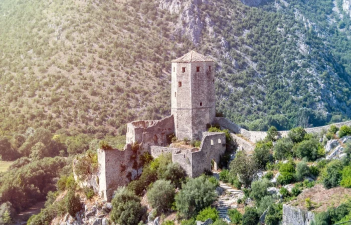 Historic Počitelj fortress with a prominent stone tower and medieval walls set on a green hillside above the Neretva Valley in Bosnia and Herzegovina.