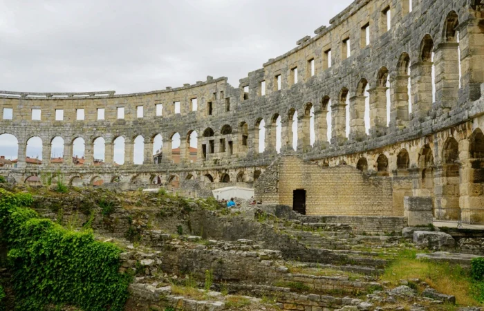 Interior view of the Pula Arena, a massive Roman amphitheatre in Croatia, with ancient stone arches, ruins, and green vegetation - iconic landmark and major historical attraction in Pula, Istria.