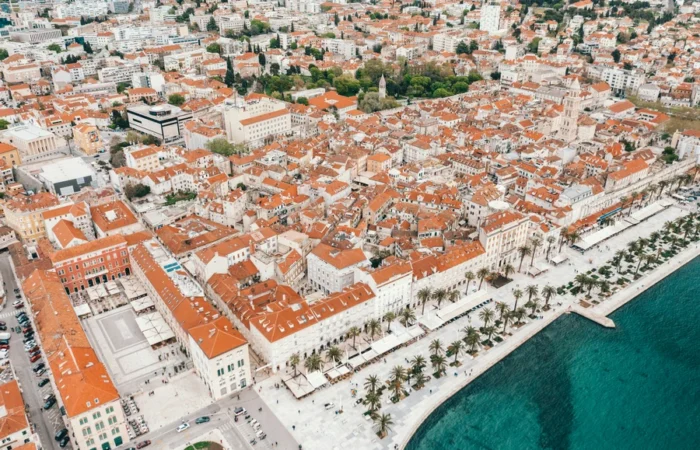 Aerial photo of Split, Croatia, featuring the UNESCO-listed Diocletian’s Palace with its maze of terracotta rooftops, palm-lined Riva promenade, and turquoise Adriatic shoreline.