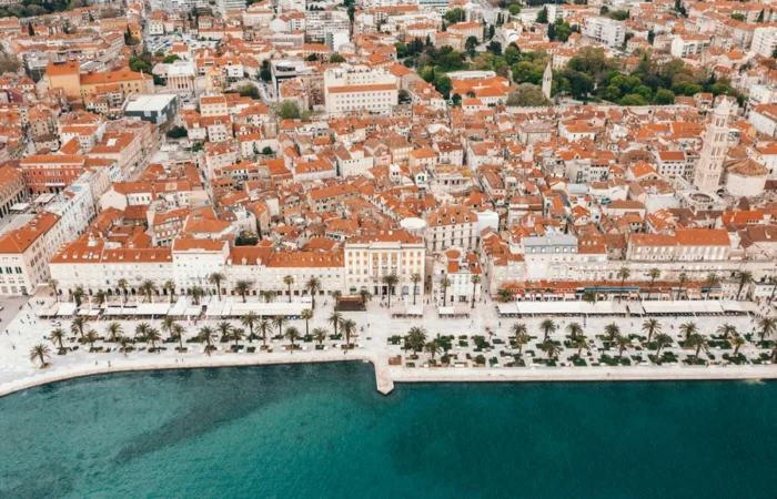 Aerial view of Diocletian’s Palace and the Split Riva waterfront with palm-lined promenade and terracotta rooftops - iconic UNESCO landmark and must-see attraction in Split, Croatia.