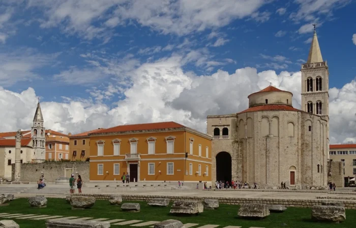 View of the Roman Forum and Church of St. Donatus in Zadar, Croatia, with ancient stone remains, historic buildings, and the iconic bell tower under a dramatic sky - must-see landmark and symbol of Zadar’s heritage.