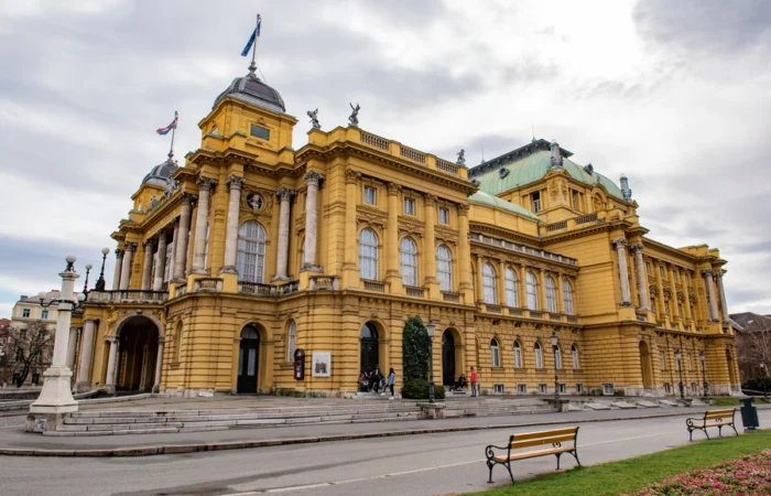 The Croatian National Theatre in Zagreb, Croatia - grand neo-baroque building with ornate façades, distinctive yellow color, and national flags, set on a landscaped city square.
