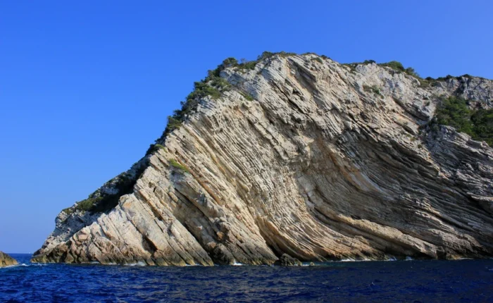 Dramatic diagonal white limestone cliffs of Strmac rising from deep blue Adriatic waters on Biševo Island, Croatia, with sparse greenery under a clear sky.