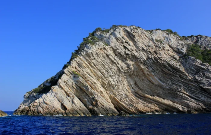 Dramatic diagonal white limestone cliffs of Strmac rising from deep blue Adriatic waters on Biševo Island, Croatia, with sparse greenery under a clear sky.