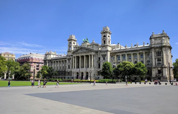 Budapest’s grand Museum of Ethnography with ornate neoclassical façade, green lawns, and pedestrians in Kossuth Square under a clear blue sky.