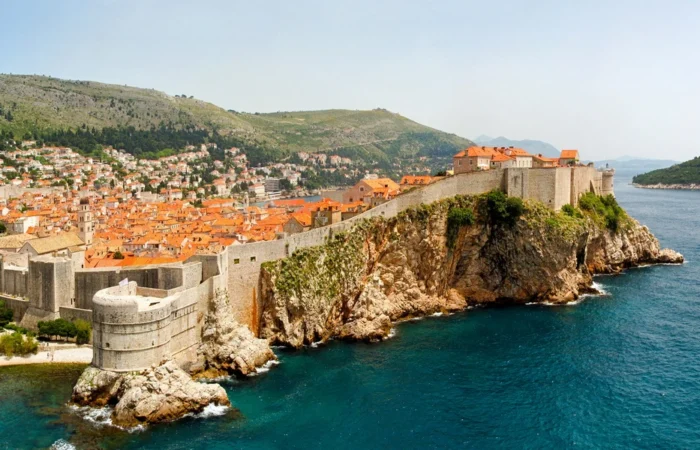 Panoramic view of Dubrovnik’s historic stone walls perched on cliffs above the Adriatic, orange rooftop old town, Mt. Srđ in the background, and Lokrum Island on the horizon.