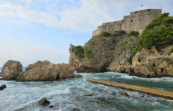 Lovrijenac Fort perched atop rocky cliffs in Dubrovnik, recognized as the Red Keep of King’s Landing in Game of Thrones, with crashing waves and lush greenery.