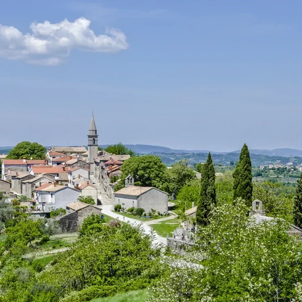 Scenic view of the medieval hilltop town of Hum in Istria, Croatia, with red-roofed houses, a church steeple, and lush green countryside on a sunny day.