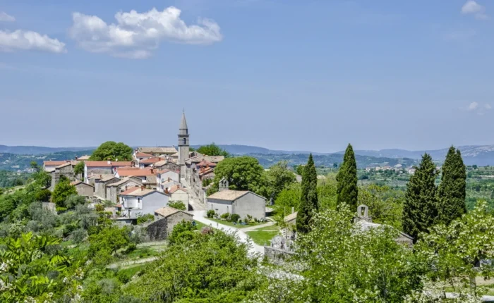 Scenic view of the medieval hilltop town of Hum in Istria, Croatia, with red-roofed houses, a church steeple, and lush green countryside on a sunny day.