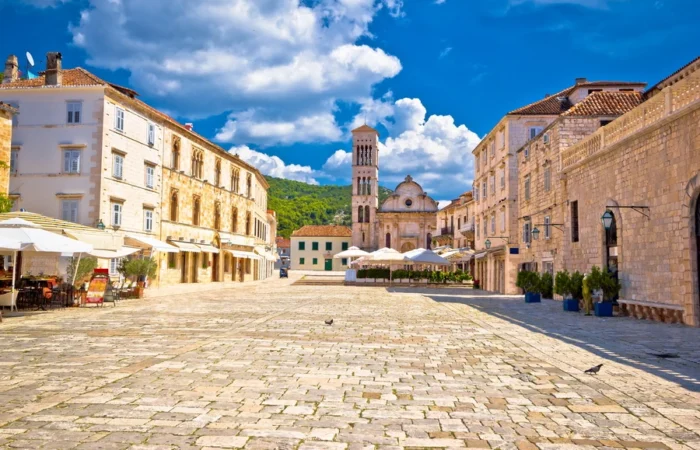 Sunny view of Hvar’s spacious stone-paved main square with al fresco cafes, the historic Cathedral of St. Stephen, and elegant Venetian-style buildings.