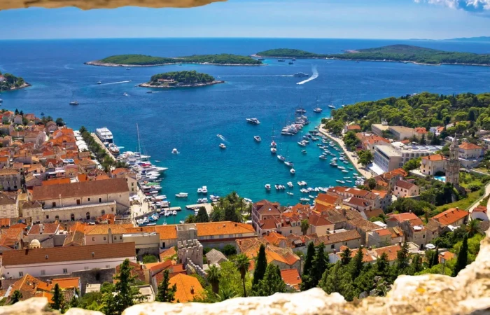 Spectacular view of Hvar Town’s terracotta rooftops, marina full of boats, and the blue Adriatic dotted with Pakleni Islands, seen through an old fortress window.