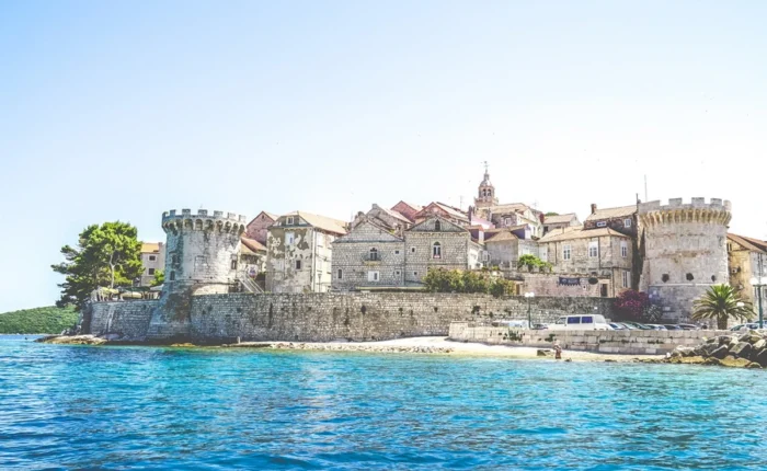 Medieval fortress towers and stone walls of Korčula Old Town, Croatia, seen from the Adriatic, with historic architecture and crystalline blue water.
