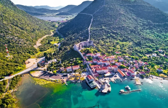 Aerial view of Mali Ston, Croatia, with medieval defensive walls running over hills, red-roofed houses, turquoise bay, and famous oyster farms.