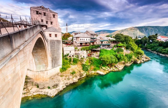 Close-up view of Mostar’s Stari Most (Old Bridge) arching over the turquoise Neretva River, with historic stone buildings and dramatic Balkan hills in Bosnia and Herzegovina.