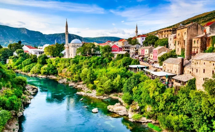 Panoramic view of Mostar Old Town with mosque minarets, colorful Ottoman houses, and the emerald Neretva River flowing through lush greenery in Bosnia and Herzegovina.
