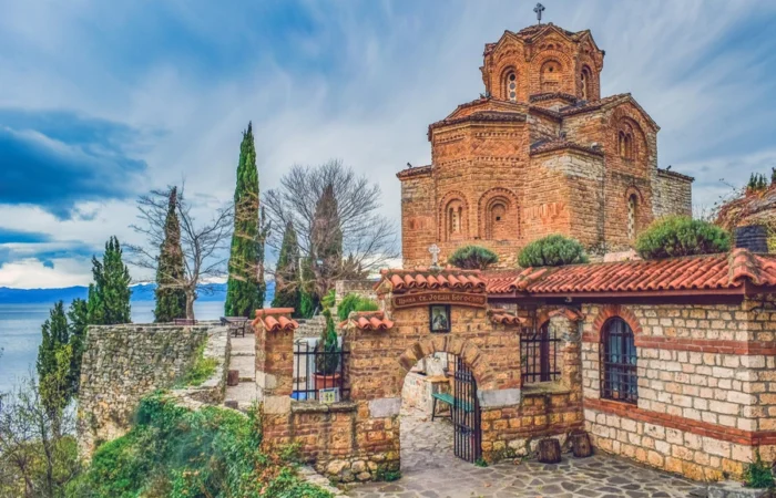 Church of St. John at Kaneo sits atop a cliff overlooking Lake Ohrid, surrounded by cypress trees and dramatic sky in North Macedonia.