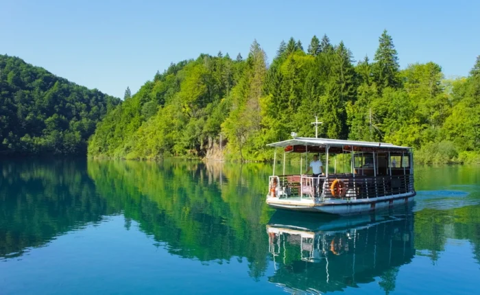 Close-up of electric sightseeing boat cruising on the blue-green lake surrounded by lush forest in Plitvice Lakes National Park, Croatia.