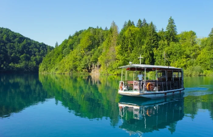 Close-up of electric sightseeing boat cruising on the blue-green lake surrounded by lush forest in Plitvice Lakes National Park, Croatia.