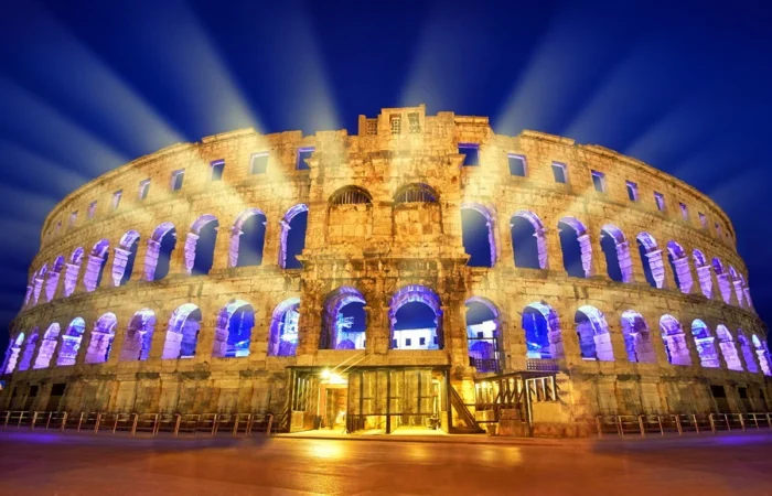 Pula Arena’s Roman arches beautifully illuminated with blue and gold lights, creating a spectacular night scene in Croatia.