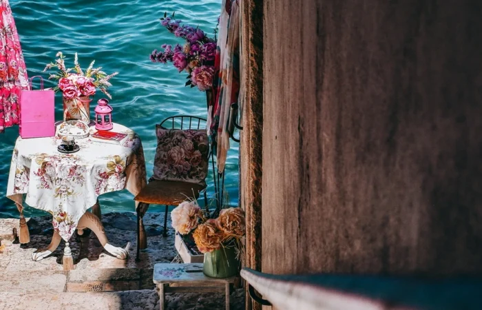 Artistic vintage café table with floral decorations set beside a stone wall just above the blue Adriatic waters in Rovinj, Croatia.