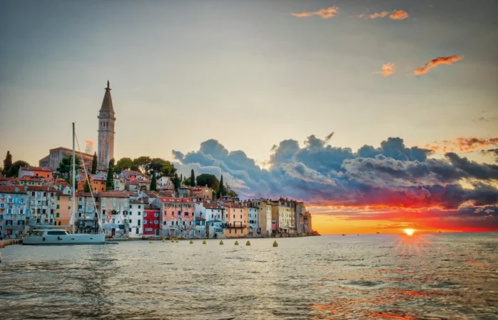 Rovinj’s old town and St. Euphemia church viewed from the sea at sunset, with a yacht in the foreground and glowing colors in the Adriatic sky, Croatia.