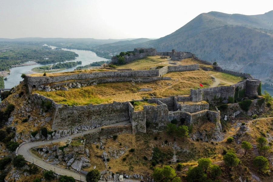 Aerial view of Rozafa Castle near Shkoder, Albania with its ancient stone walls perched atop a hill overlooking winding rivers and distant mountains.