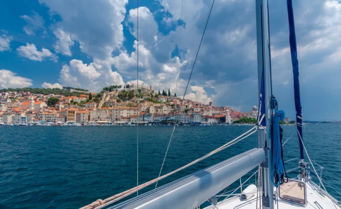 View of Šibenik old town with its waterfront, colorful houses, St. Michael’s fortress, and the dome of St. James Cathedral from a sailboat on the Adriatic.