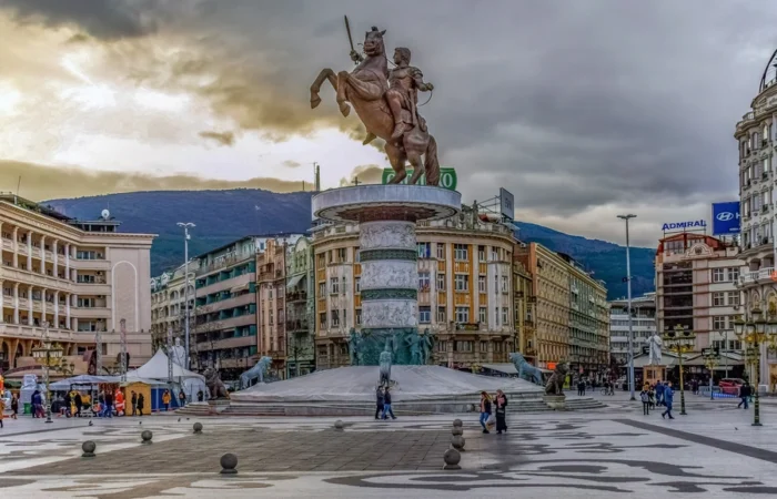 Monumental "Warrior on a Horse" statue, depicting Alexander the Great, stands atop a marble fountain in Skopje's Macedonia Square against a dramatic sky.