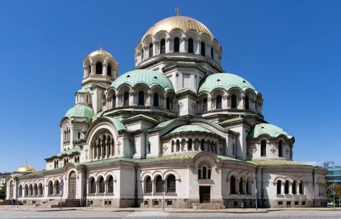 Front view of the iconic Alexander Nevsky Cathedral in Sofia, Bulgaria, with golden and green domes shining under a clear blue sky.