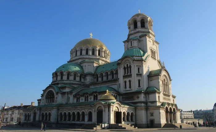 Low-angle morning view of Alexander Nevsky Cathedral in Sofia, Bulgaria, with golden domes illuminated by sunlight and a clear sky.