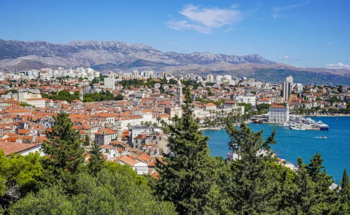 View across the green slopes of Marjan hill to the city of Split, with the red-tiled Old Town, Riva promenade, blue Adriatic, and city harbor.