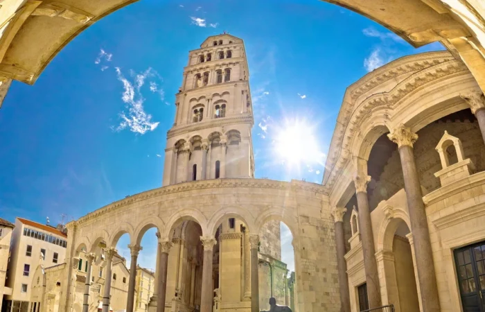 The bell tower of St. Domnius Cathedral rises above the Peristyle square and Roman arches, bathed in sunlight and framed by an arch, in Diocletian’s Palace, Split.