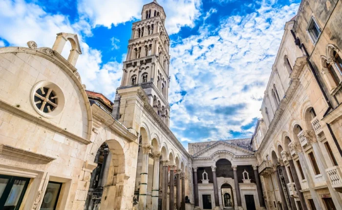 Diocletian’s Palace Peristyle square with Roman arches, columns, and the bell tower of St Domnius Cathedral under a blue sky, Split, Croatia.